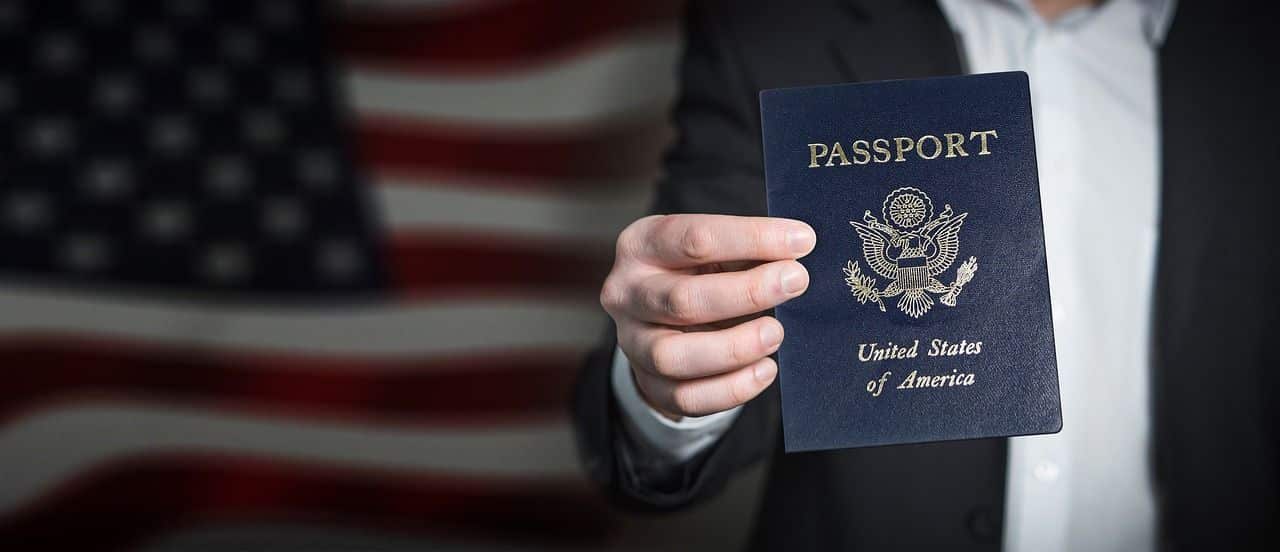 mão segurando passaporte americano com bandeira dos EUA ao fundo
